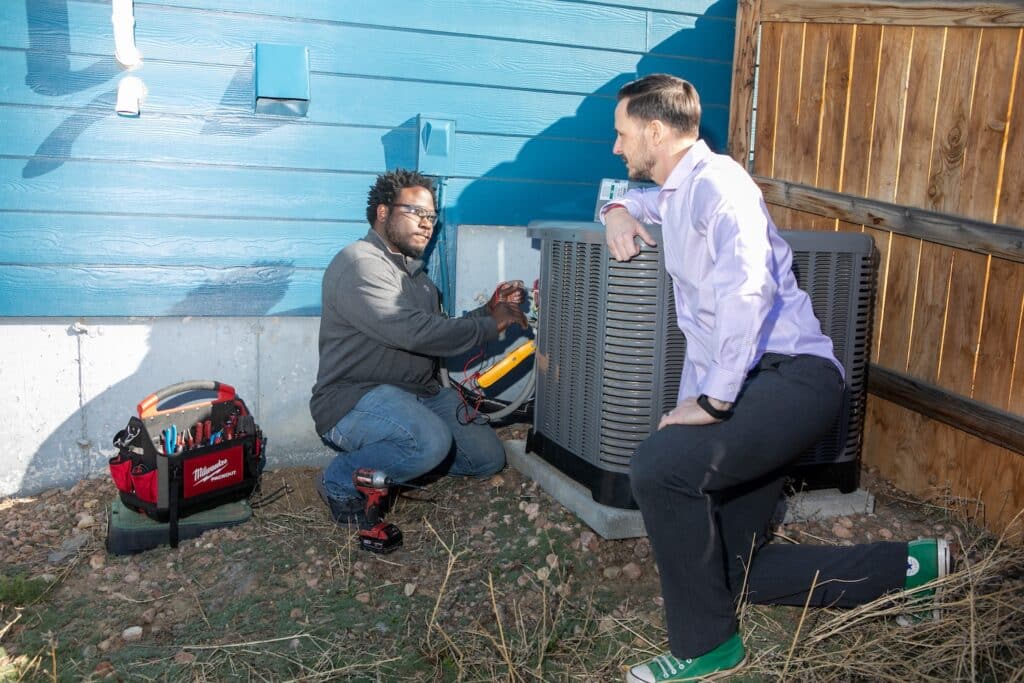 HVAC technician and homeowner outside looking at the air conditioning unit