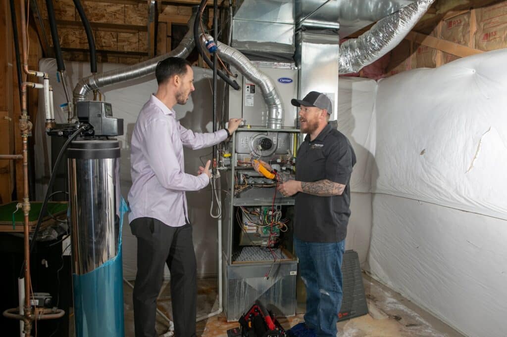 Two men talking while looking at a furnace.