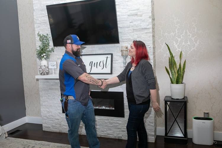 HVAC technician shaking hands with a woman in front of a fireplace